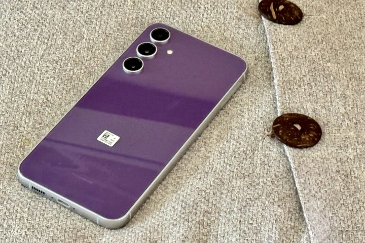 A Samsung Galaxy S23 FE in purple, showing its back, sitting on a pillow.