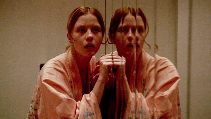 A girl knocks at a mirror door in 2018's Suspiria.