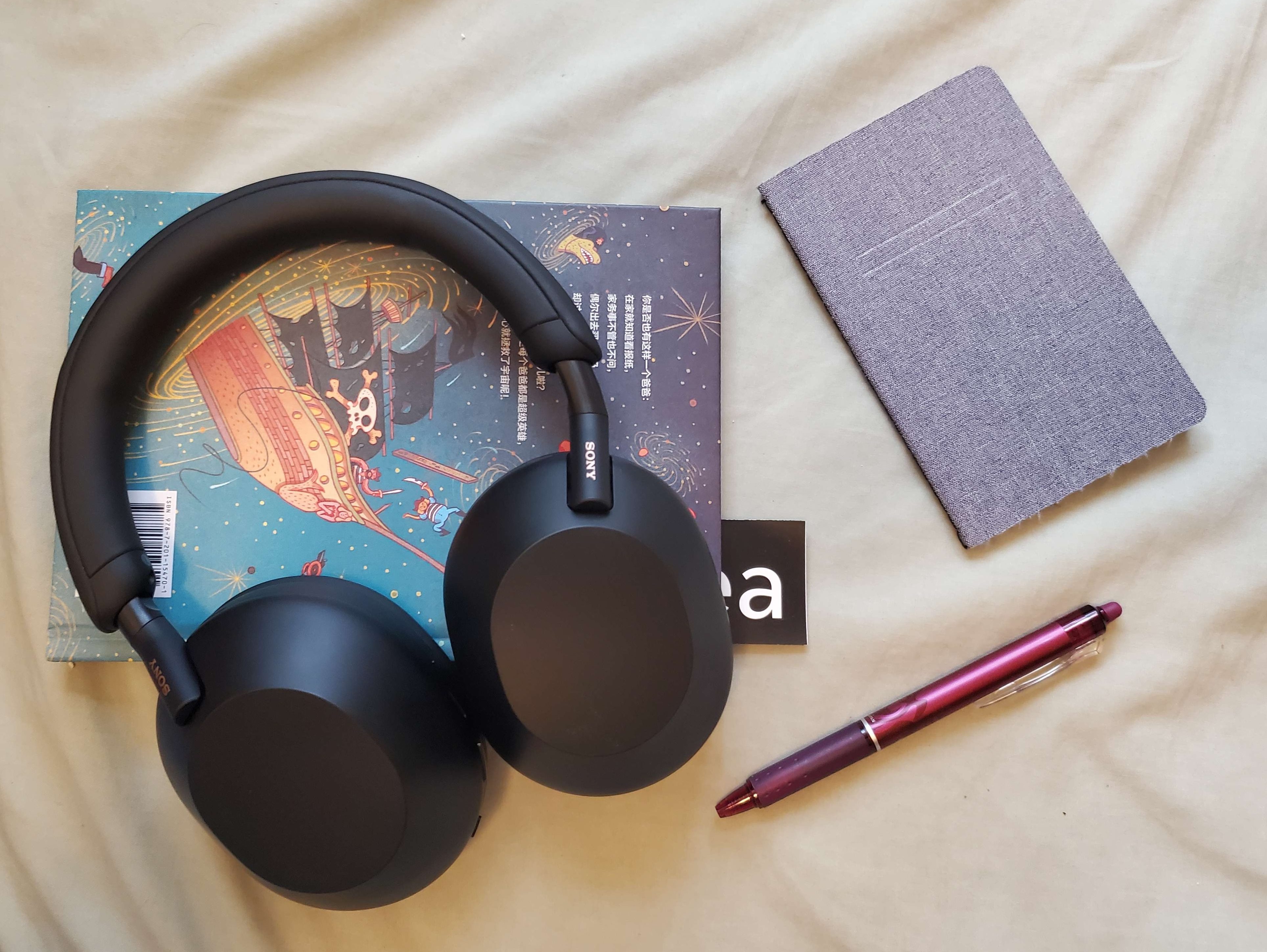 The Sony WH-1000-XM5 on top of a book for study, next to a notebook and pen.