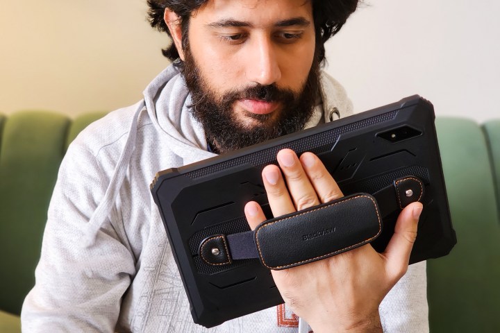 Man holds Blackview Active 8 Pro rugged Android tablet in black color by leather strap on the back.