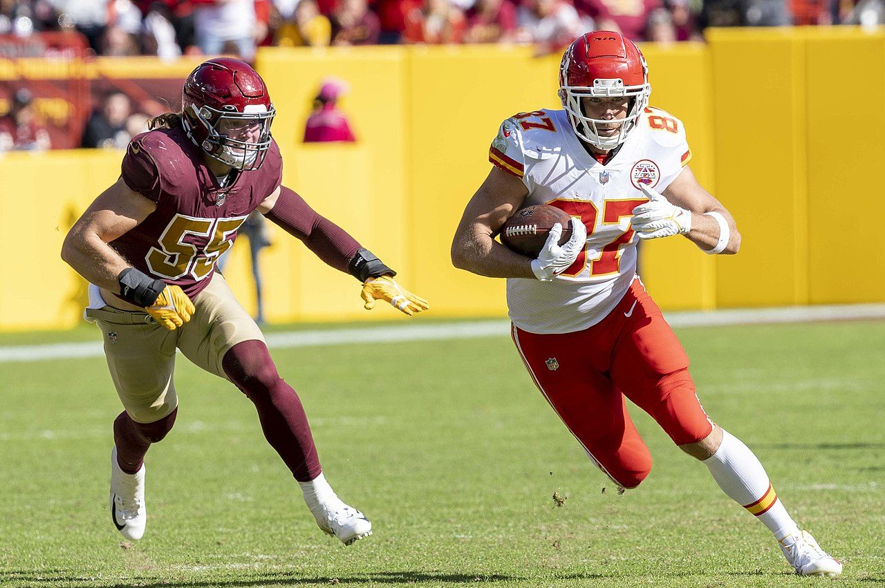 Travis Kelce runs away from a linebacker while holding the ball on the football field.