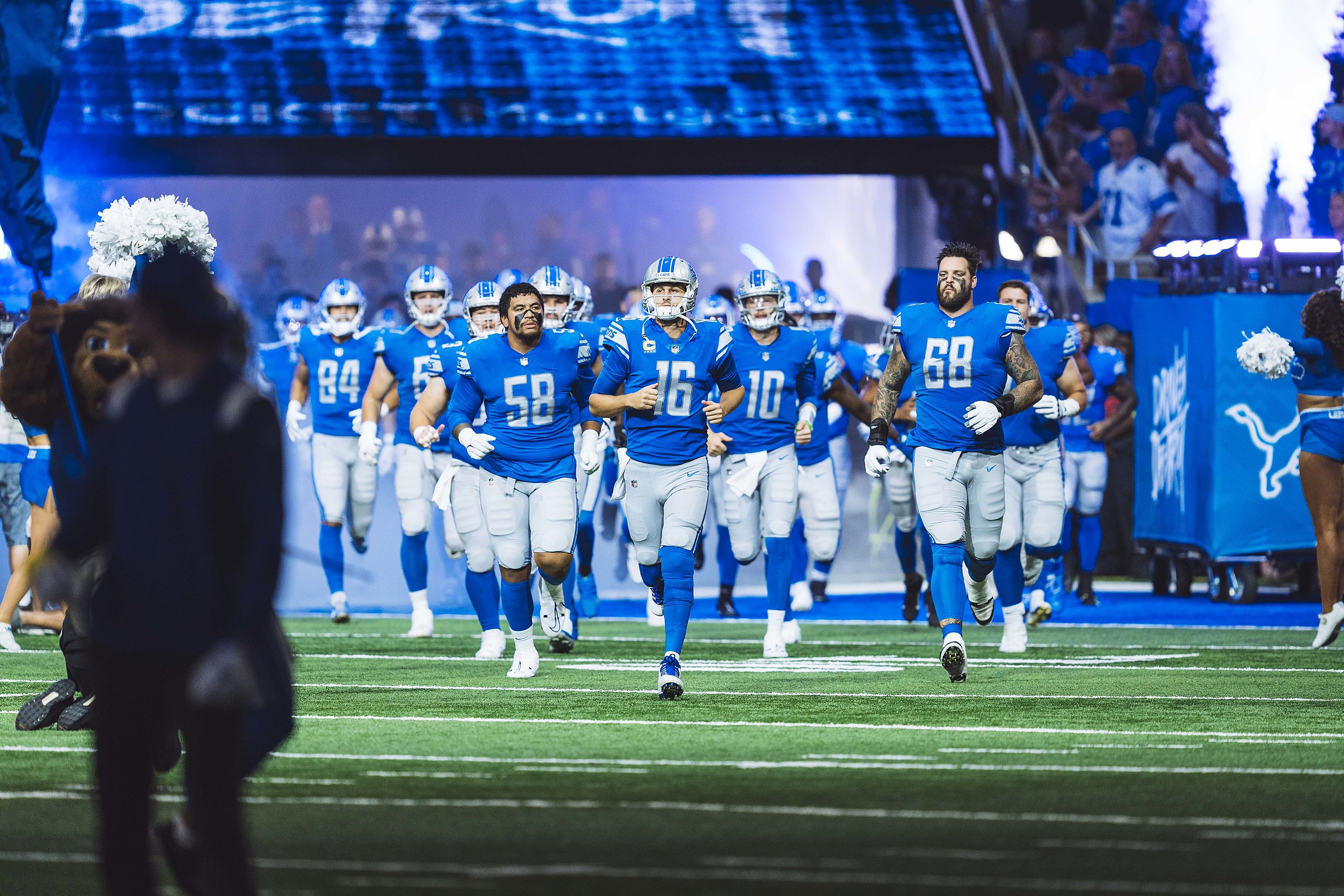 The Detroit Lion football players run out of the tunnel on a field.