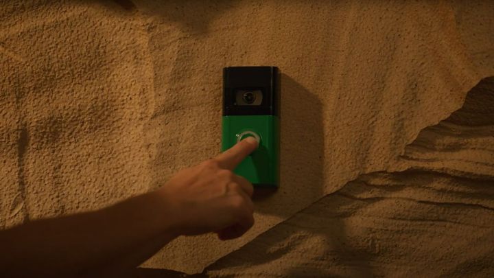 A person pressing a green Ring Video Doorbell button.