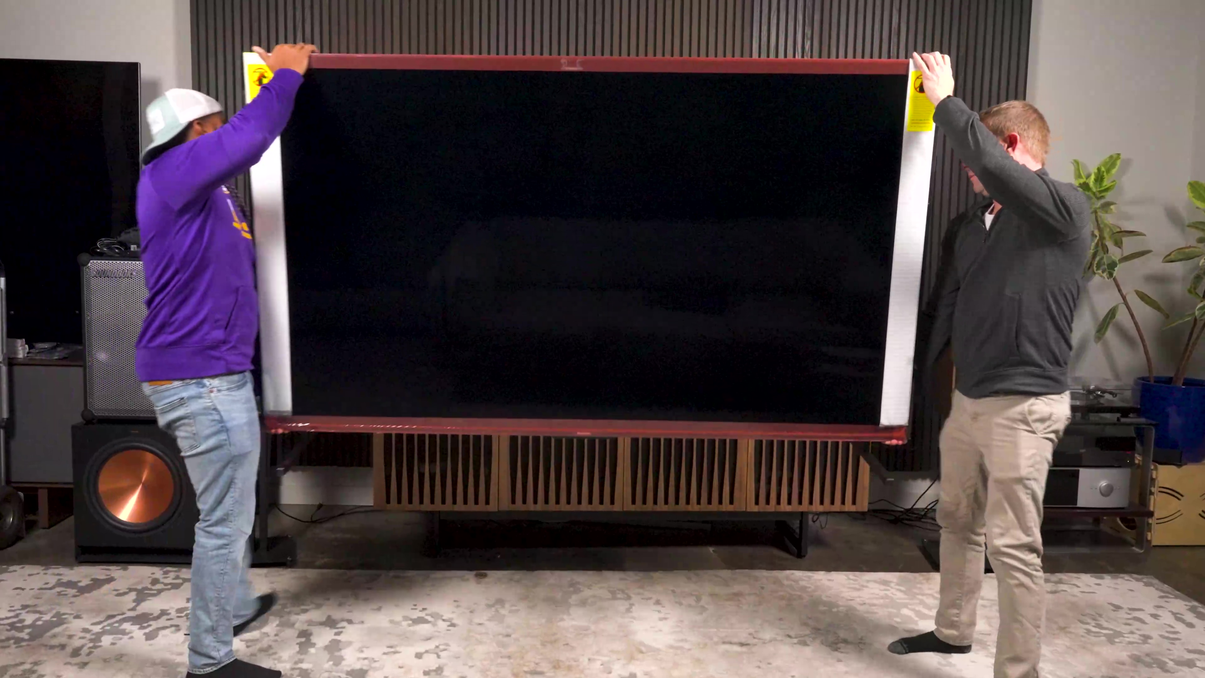 Two men lift a Hisense UX TV onto a media console. 