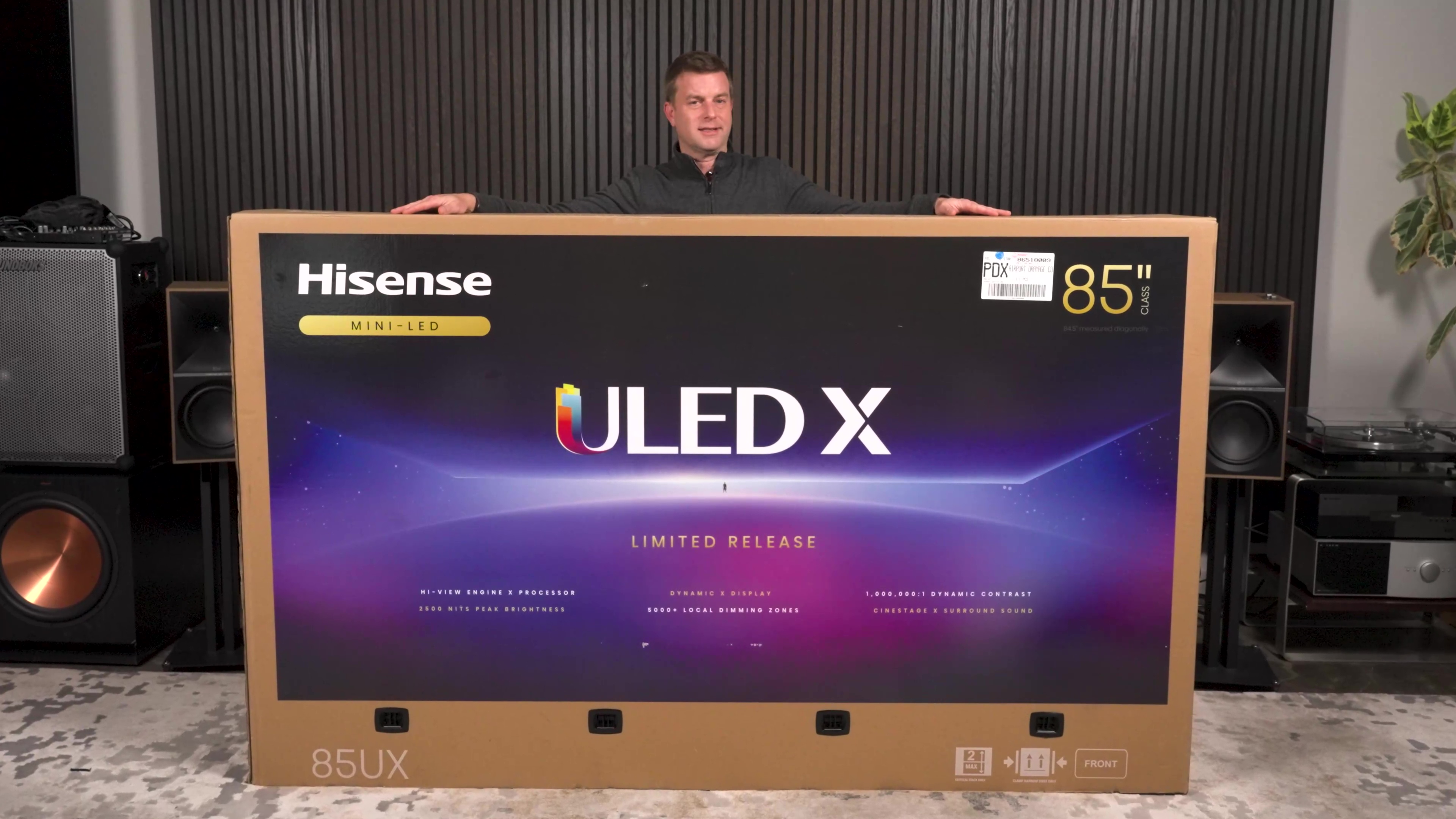 A man stands behind the huge box for a Hisense UX 85-inch TV. 