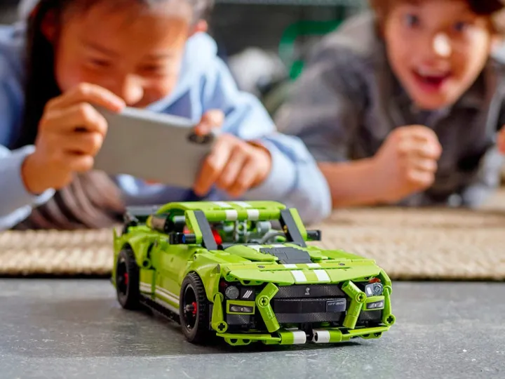 Deux enfants jouent avec la Ford Mustang Shelby GT500 Lego Technic.