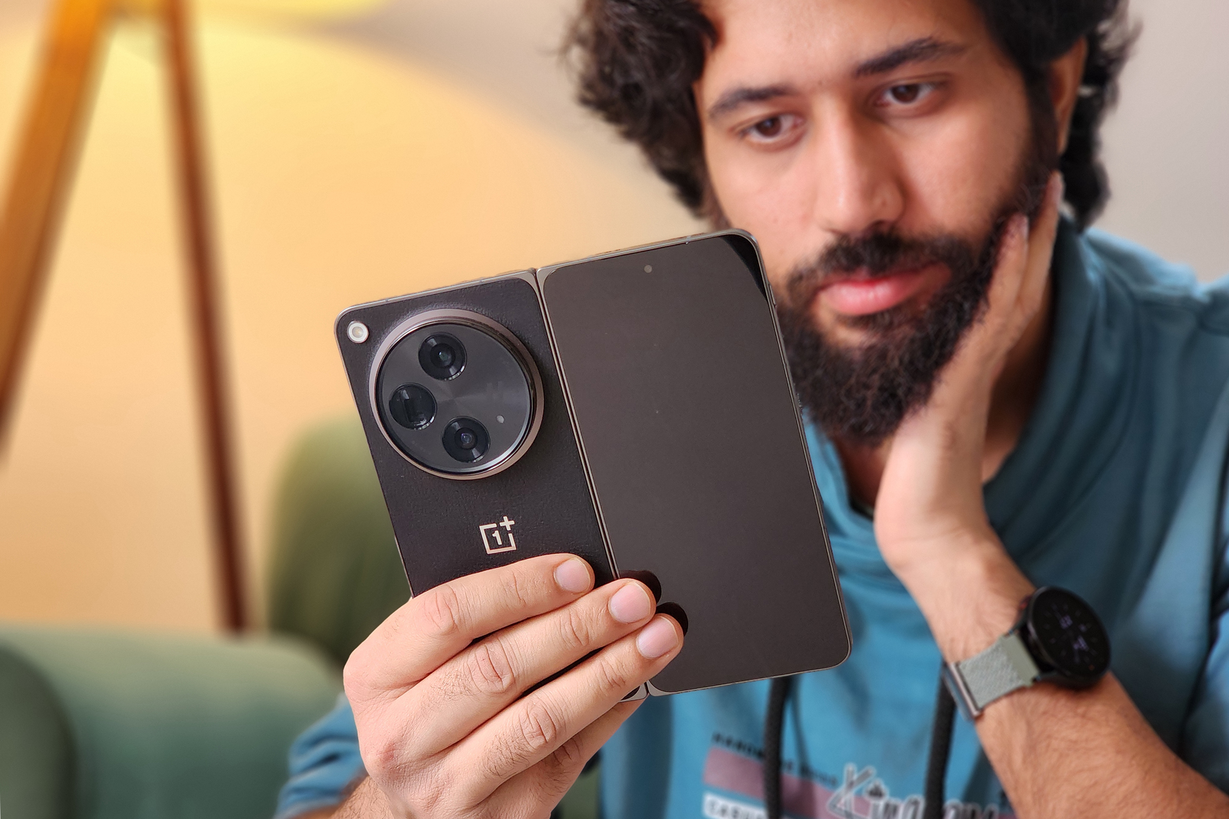 Man using OnePlus Open <a href='https://dbhmsp1982.com/affiliate-registration' target='_blank'>black</a> color with one hand while sitting on a couch.”><figcaption id=