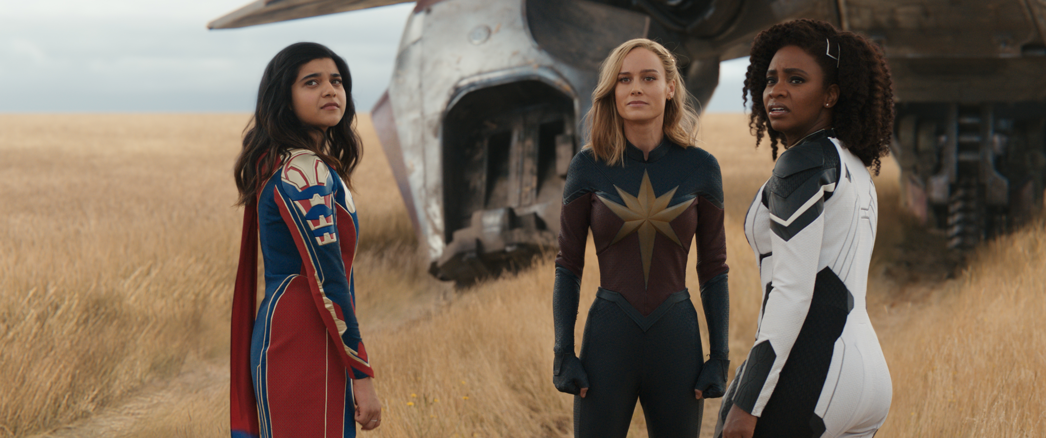 Iman Vellani, Brie Larson, and Teyonah Parris stand around a space ship.