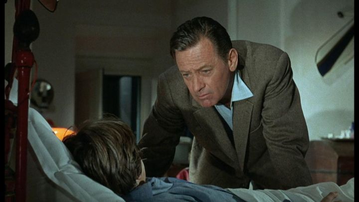 William Holden as Laurent Segúr talking to a child in bed in the film The Christmas Tree.