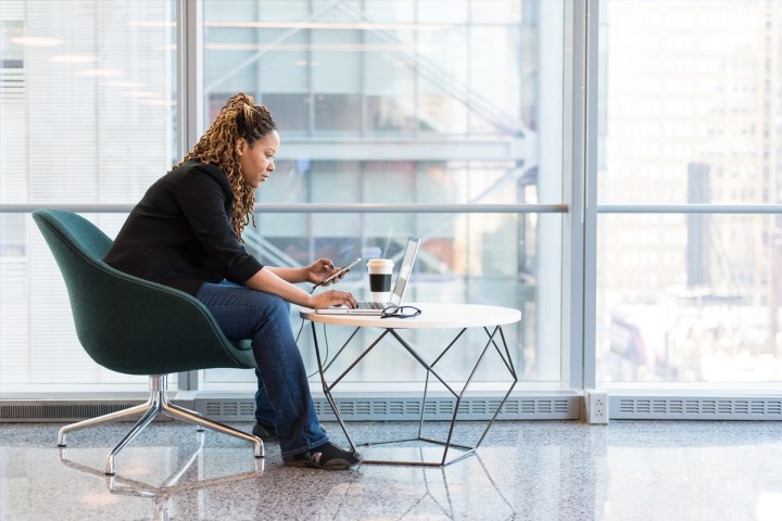 Woman leaning down to use her laptop on a low table.
