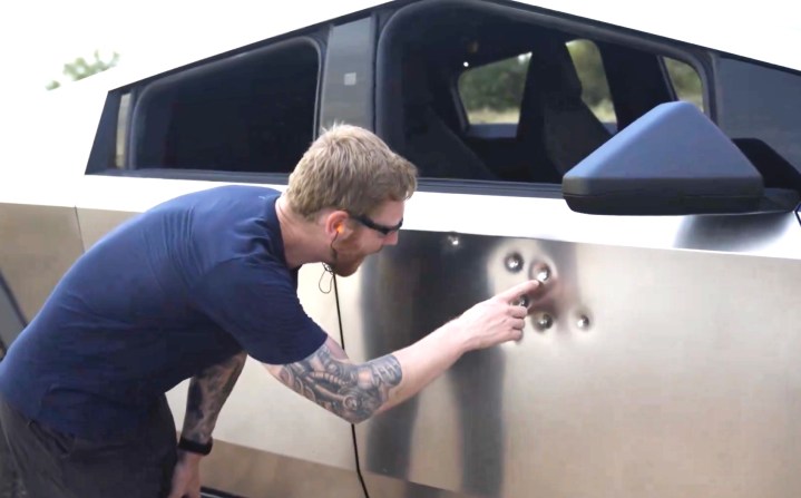 Tesla's lead Cybertruck engineer inspecting bullet damage on the new vehicle following a demonstration to highlight the strength of its exterior.