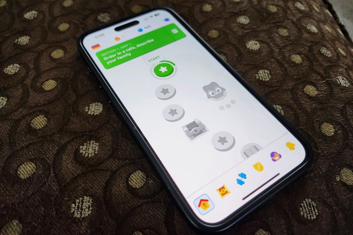 Un iPhone 15 Pro Max con l'app Duolingo appoggiata su un pouf.