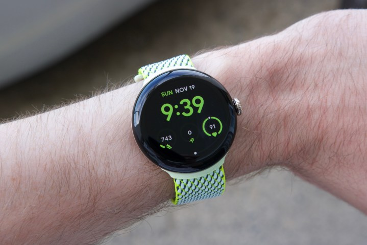 شخص يرتدي Google Pixel Watch 2 مع حزام من القماش باللون الأصفر/الأخضر.