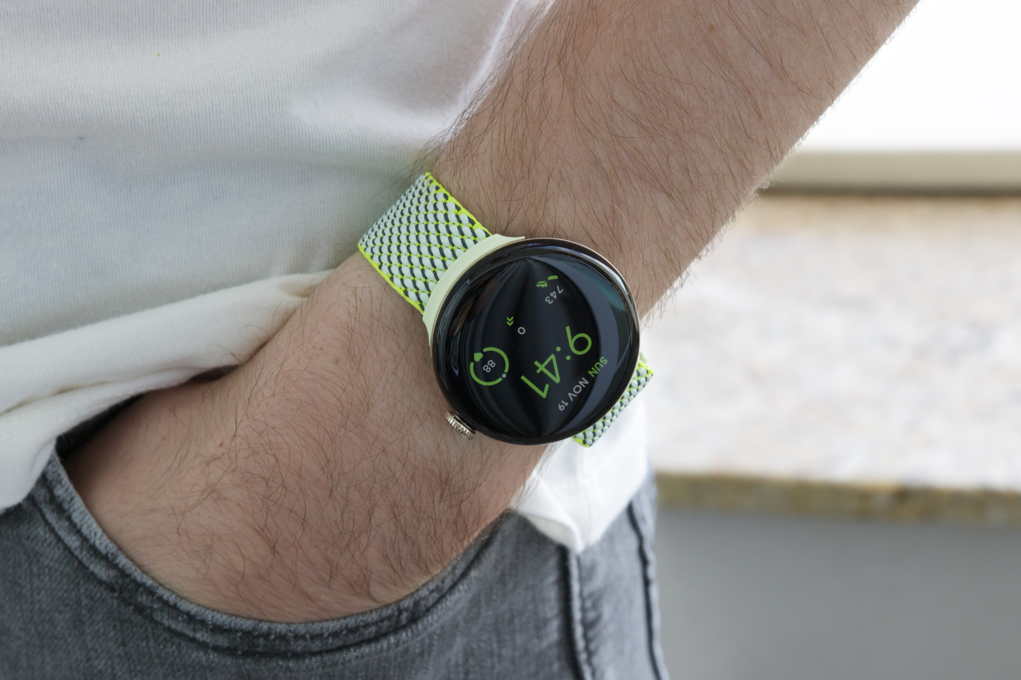 किसी ने पीले/हरे फैब्रिक बैंड वाली Google Pixel Watch 2 पहनी हुई है।
