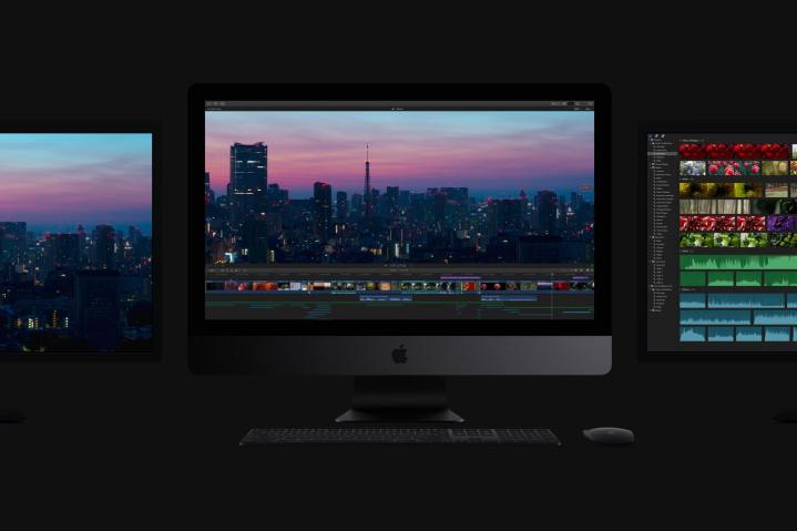 An Apple iMac Pro in a dark room flanked by two monitors, one on either side of it.