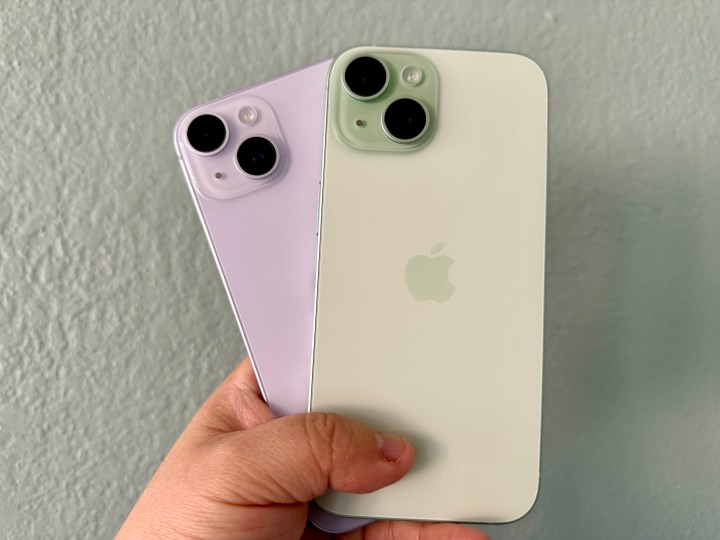 Purple iPhone 14 (left) and a green iPhone 15 in hand.