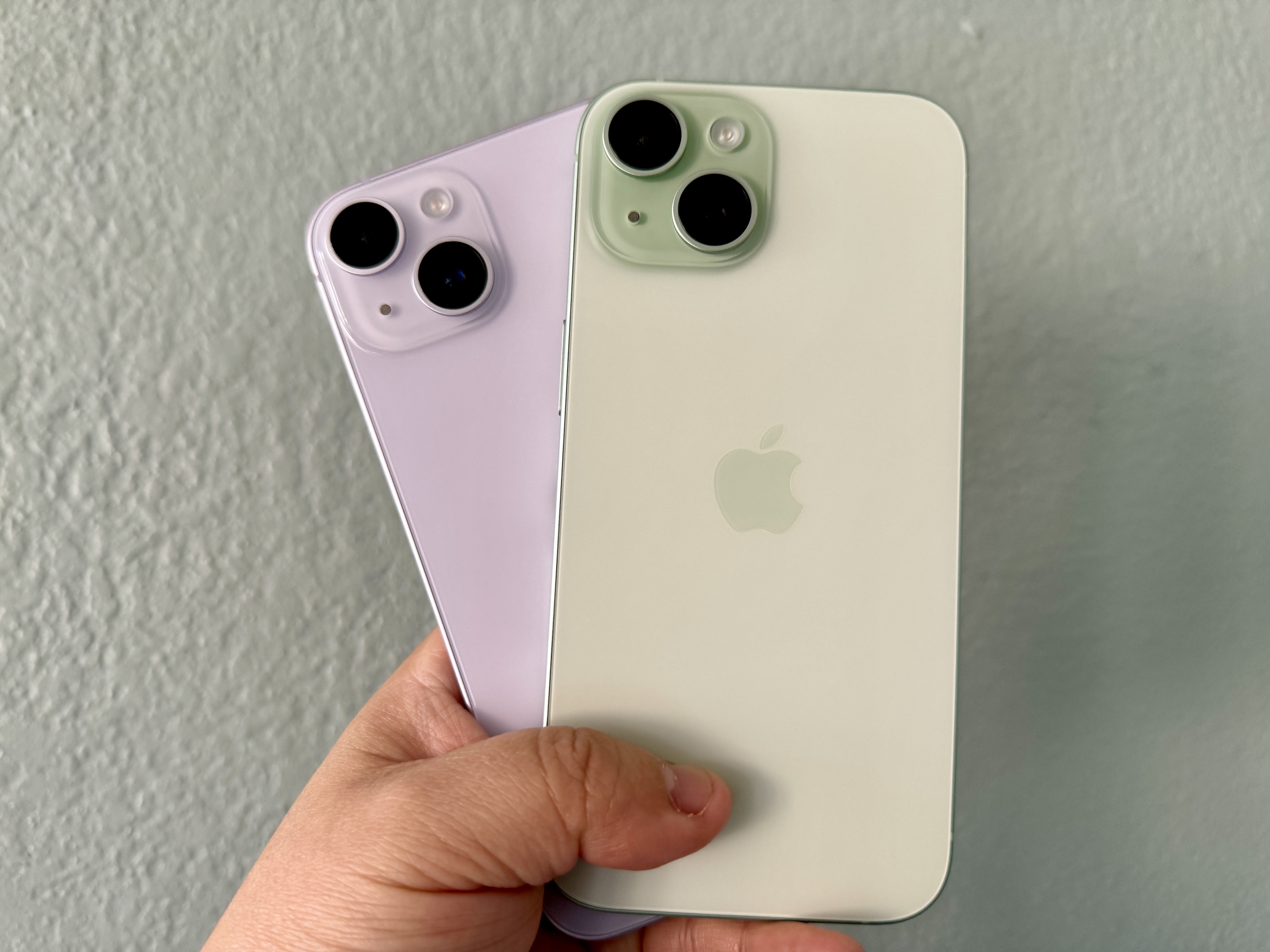 iPhone 14 morado (izquierda) y un iPhone 15 verde en la mano.