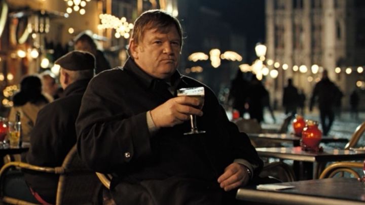 Ken drinking a beer while sitting on a table on the street in the film In Bruges,