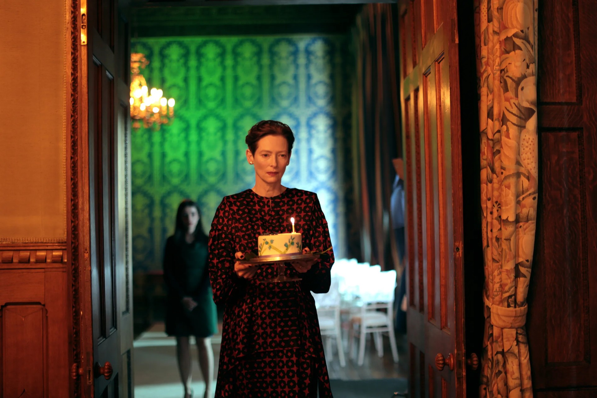 زنی با در دست داشتن کیک تولد در فیلم The Eternal Daughter قدم می زند.