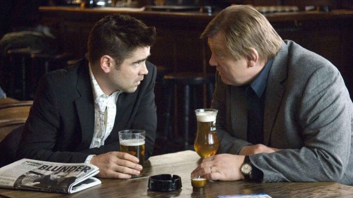 Ray and Ken talking at a pub while two beers rest on the table in front of them in the film In Bruges.