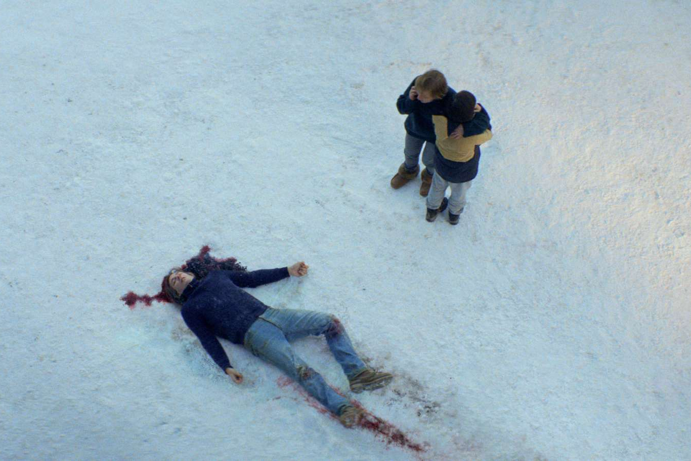 A woman and boy stare at a dead man in the snow.