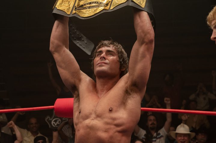 Zac Efron holds up a gold wrestling title belt in The Iron Claw.