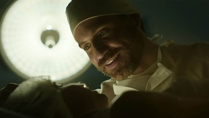 Edgar Ramirez dans le rôle de Paulo Macchiarini debout au-dessus d'un patient sur la table d'opération, souriant narquoisement dans une scène de la saison 2 de Dr. Death.