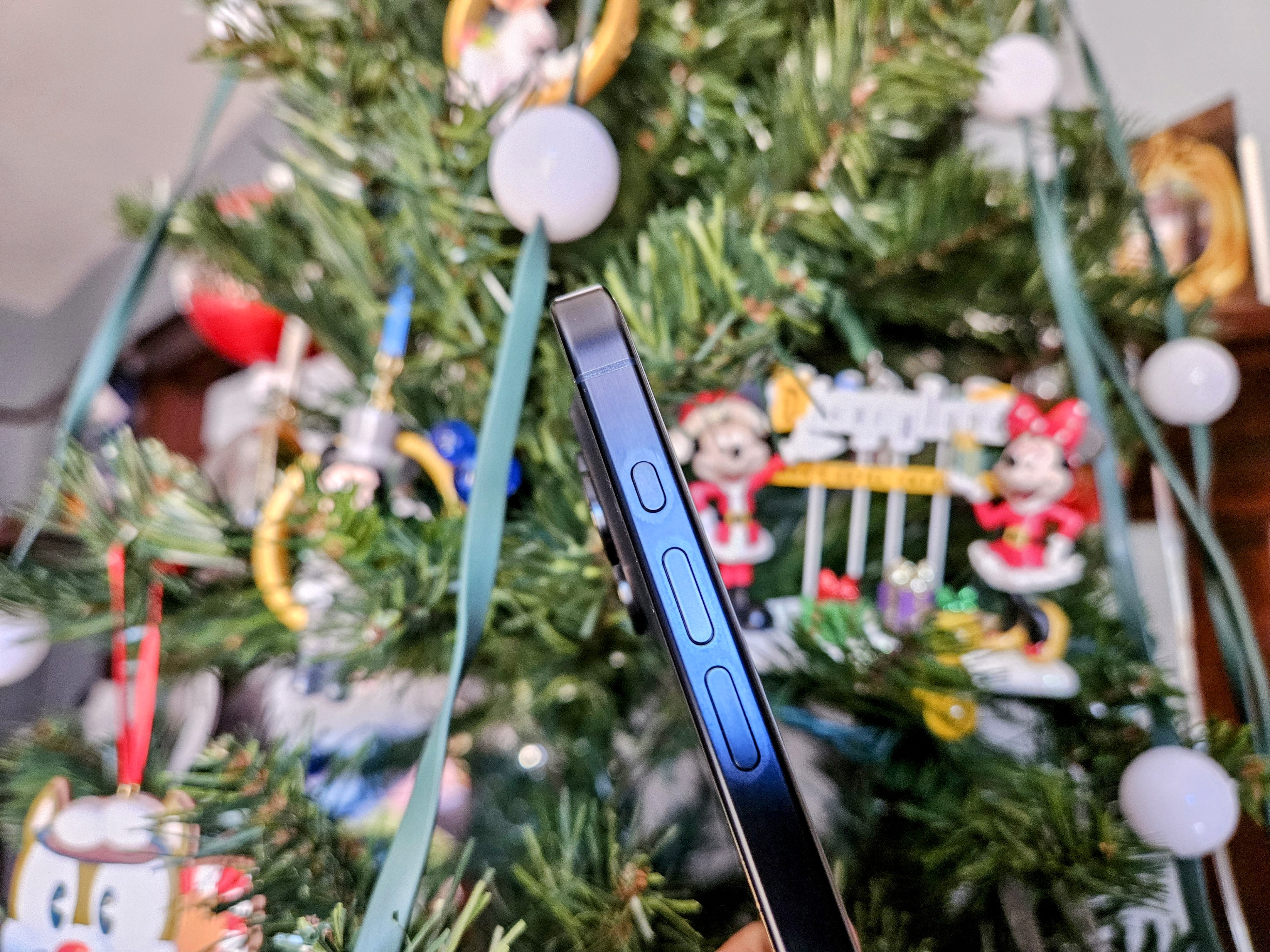 iPhone 15 Pro in Blue Titanium showing side view of Action and volume buttons in front of a Christmas tree.