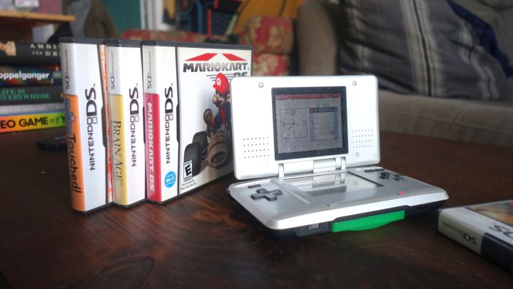 A Nintendo DS sits on a table with a few game boxes.