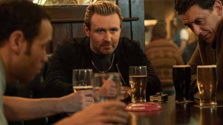 Three men at a table in a bar, one looking ahead intensely in a scene from Sexy Beast on Paramount+.