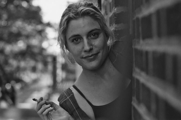 Greta Gerwig peering through a window while holding a cigarette in Frances Ha.