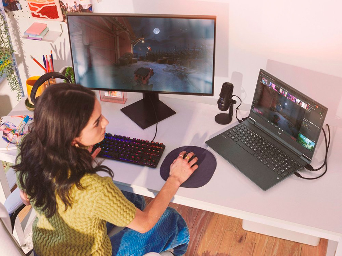 A girl plays games on the HP Victus 15.6-inch gaming laptop with a connected external display.