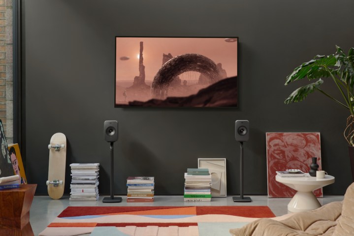 The KEF LSX II LT on stands in a setup with a TV mounted on the wall.
