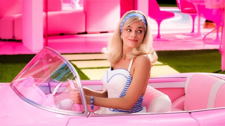 Margot Robbie como Barbie mirando hacia atrás mientras está al volante de un corvette rosa en Barbie.