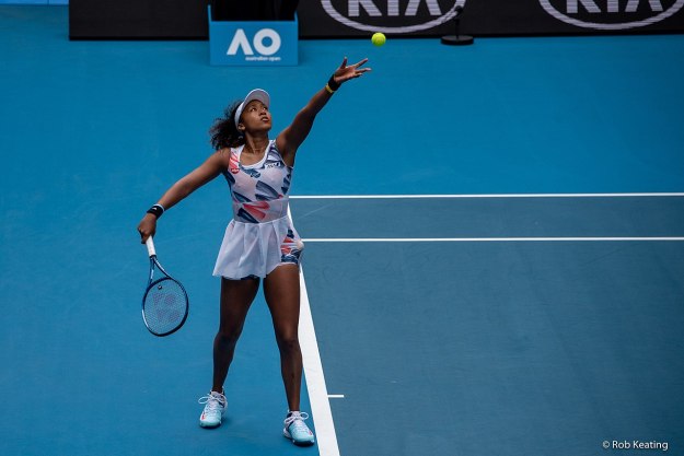 Naomi Osaka throws a tennis ball in the air.
