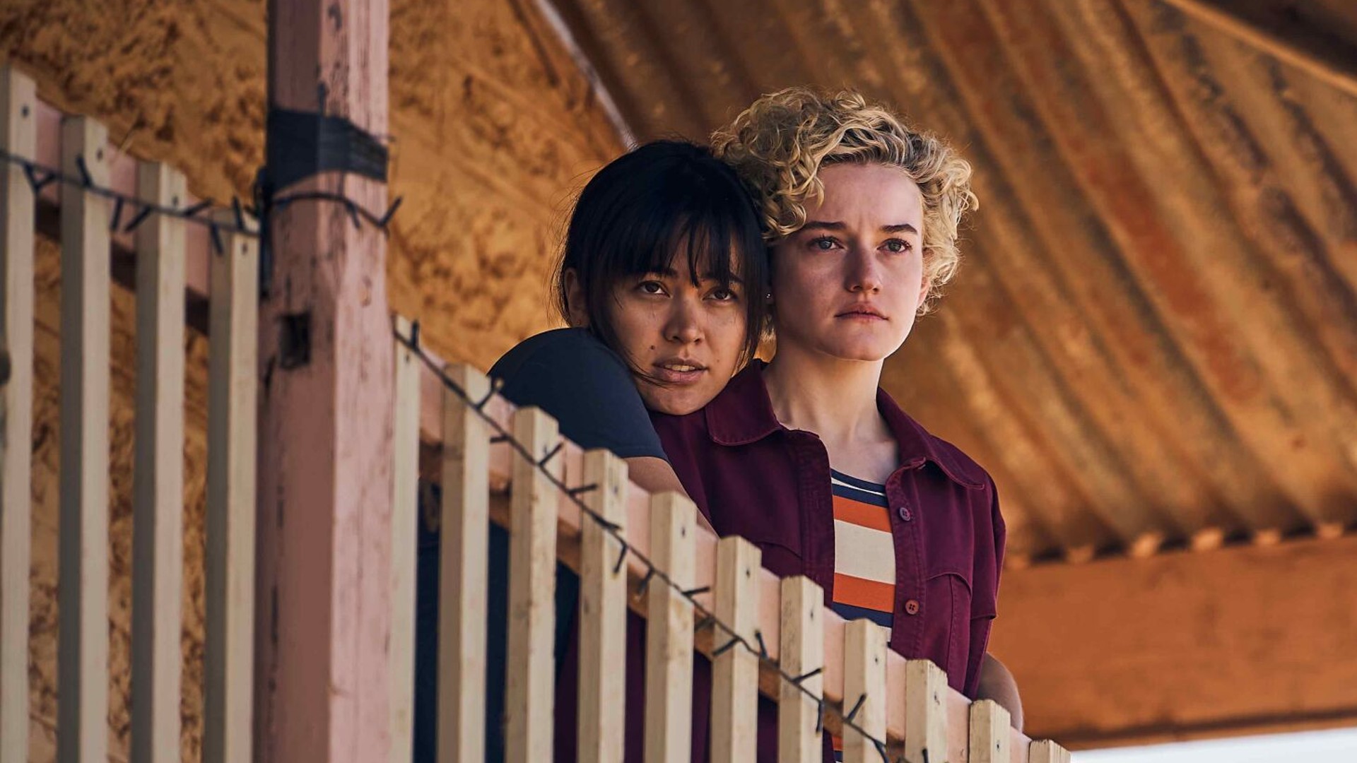 Jessica Henwick and Julia Garner hug and look out over a balcony in a still from the movie The Royal Hotel