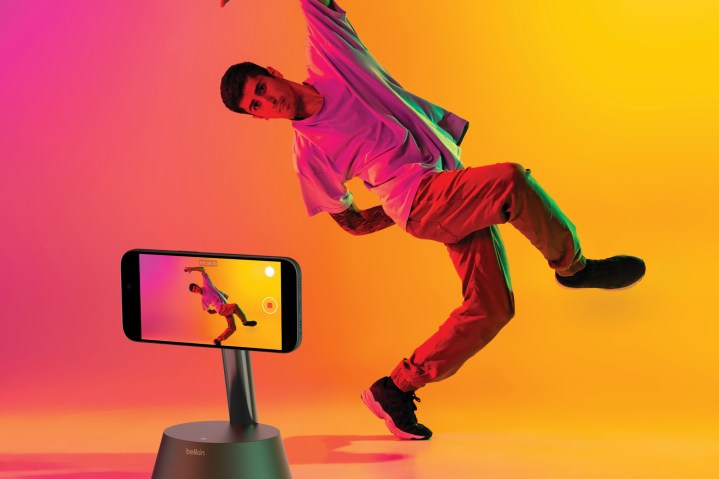 The Belkin Auto-Tracking Stand Pro being used by a man who appears to be falling over, while in a curiously painted room of orange and pink.