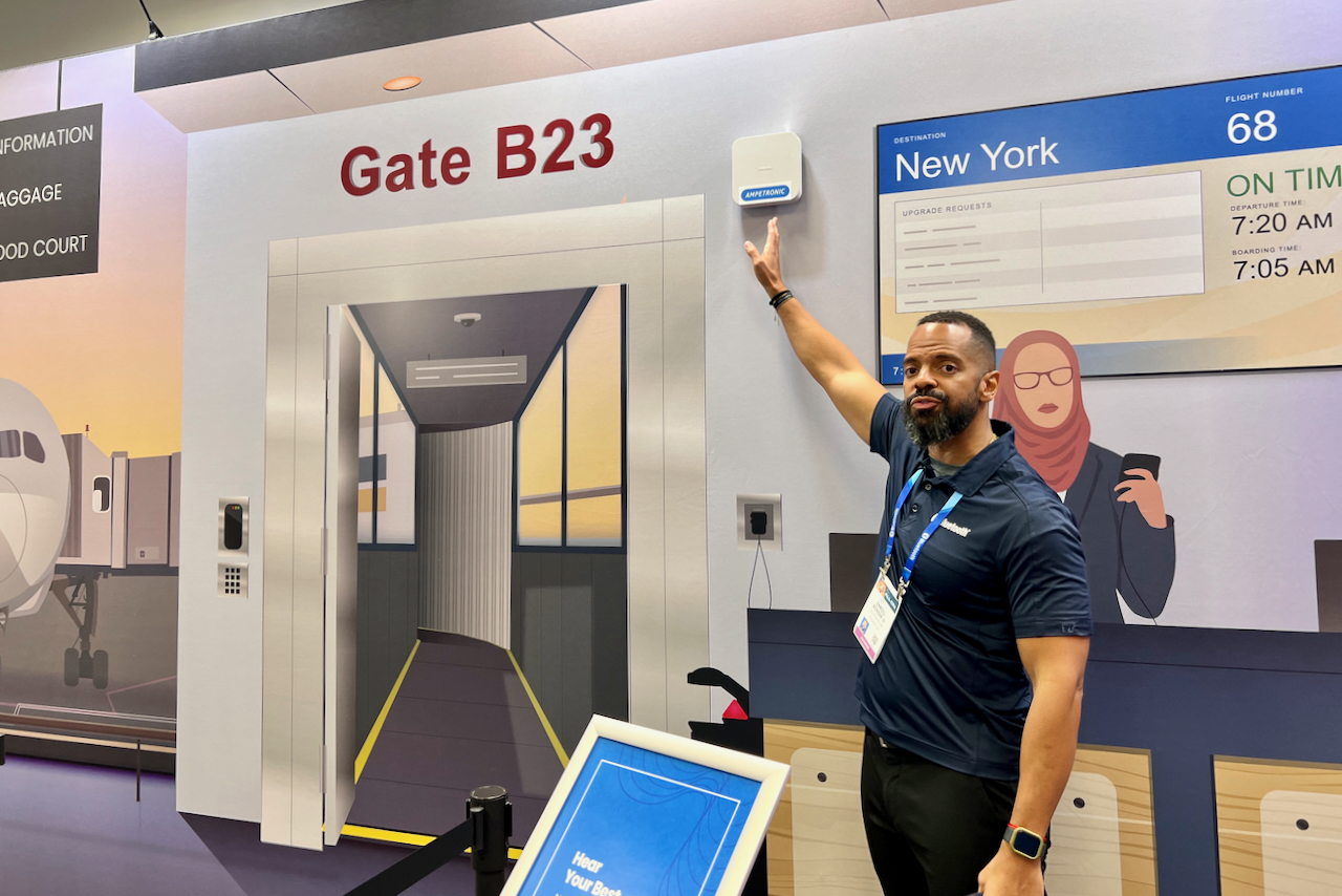 An Auracast demonstrator points to a transmitter at a mock airport gate showing the technology at CES 2024.