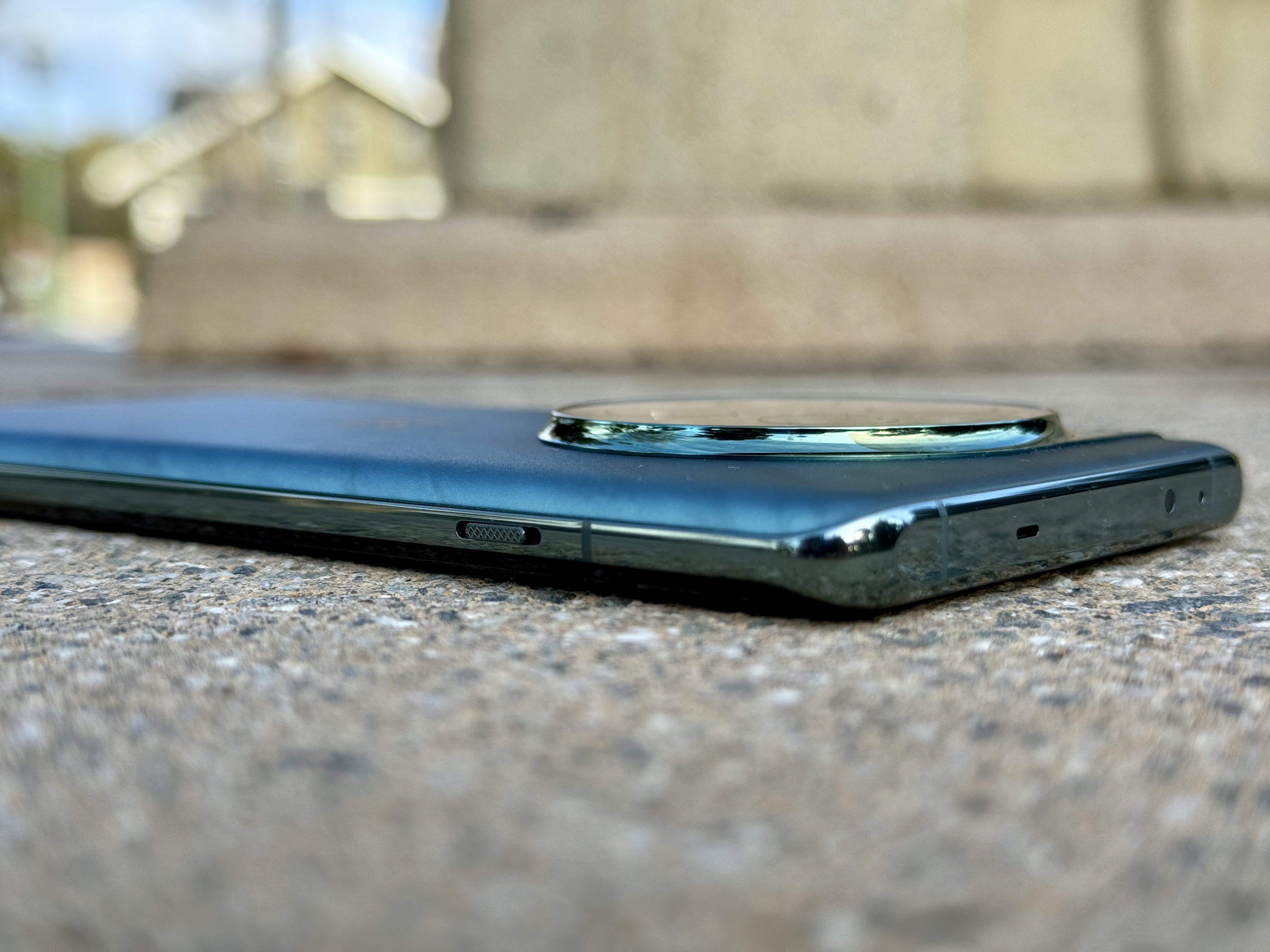 OnePlus 12 Flowy Emerald flat on surface showing angled view of alert slider and flat top edge.