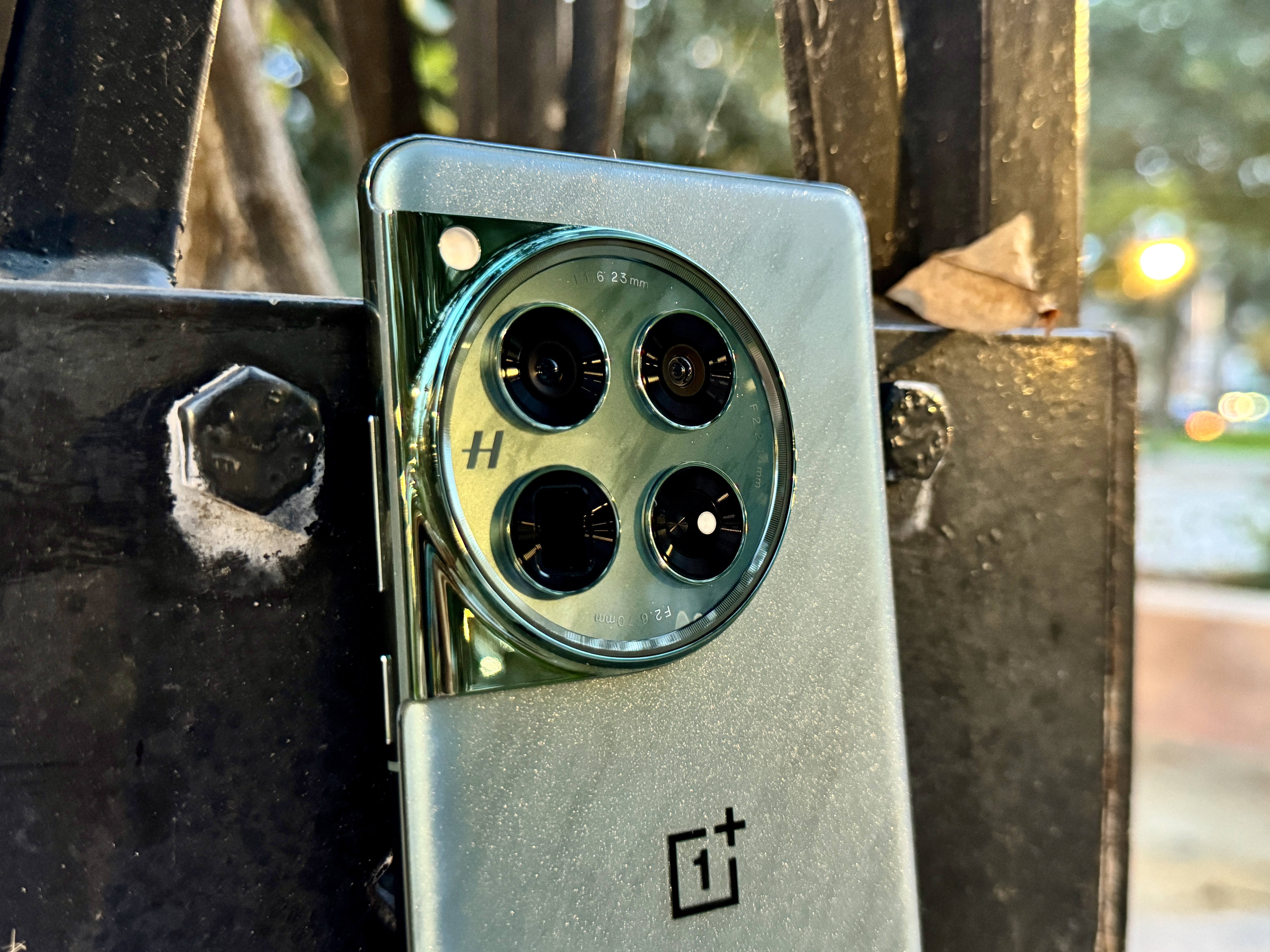 OnePlus 12 Flowy Emerald encostado em uma postagem mostrando close do módulo da câmera.