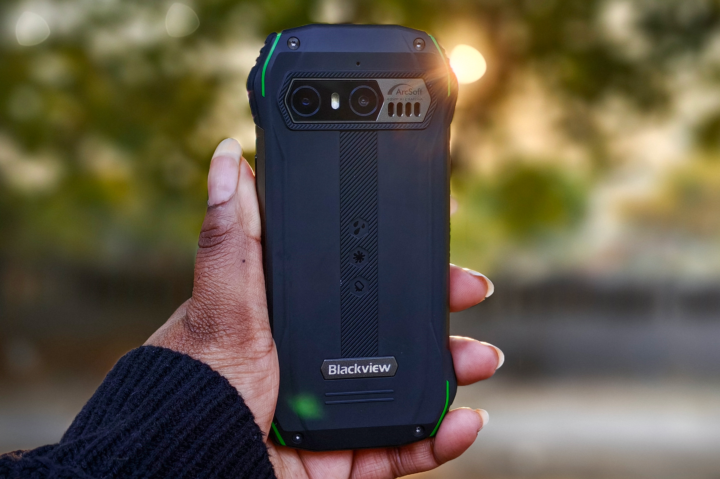 Person holding Blacview N6000 tiny rugged Android phone in hand against setting sun peaking through trees.