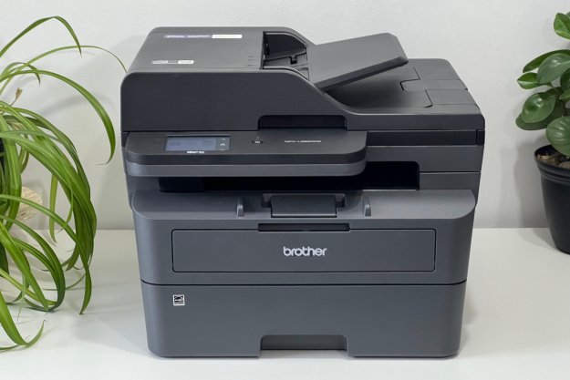 Brother's MFC-L2820DWXL laser printer rests on a white table with plants.