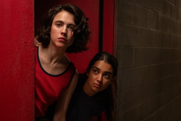 Margaret Qualley and Geraldine Viswanathan peer around a corner in a still from Drive Away Dolls