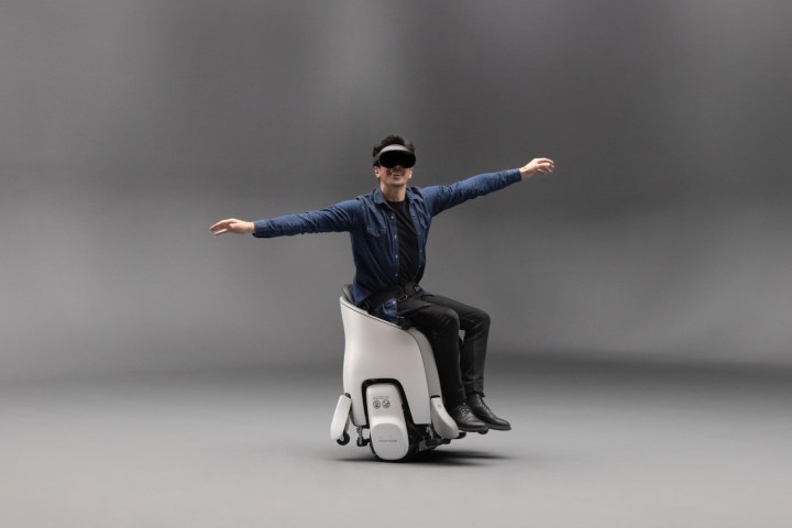 Una persona sentada en un Honda Uni-One con un casco de realidad virtual con los brazos extendidos en una posición de vuelo simulado.