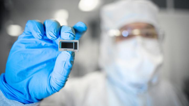 An Intel Foundry employee holds a chip between fingertips.