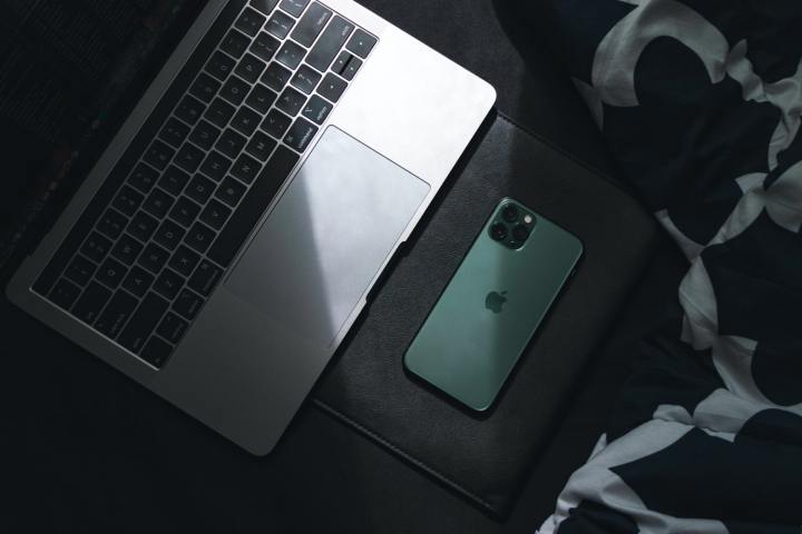 Un MacBook y un iPhone en la sombra sobre una superficie.