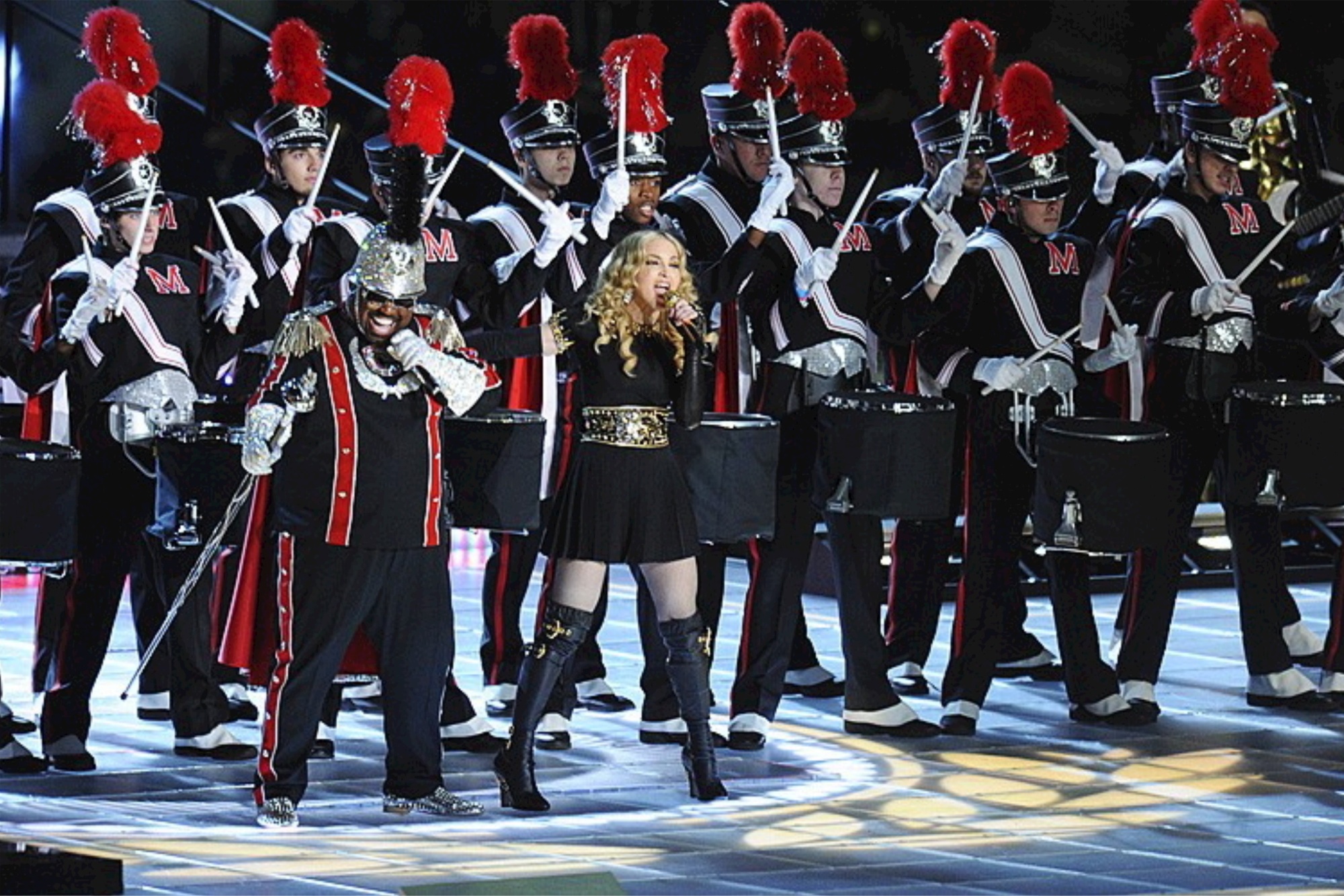 Madonna stands in front of a band and conducts.