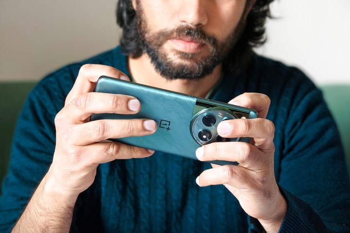 مردی که یک گوشی سبز رنگ OnePlus 12 را در دستان خود در حالی که مشغول بازی است.