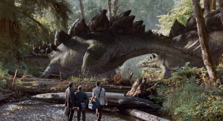 Three people stand in front of dinosaurs.