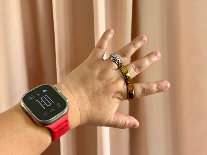 Apple Watch Ultra با بند مچی قرمز با حلقه Movano Evie و Oura در انگشتان.